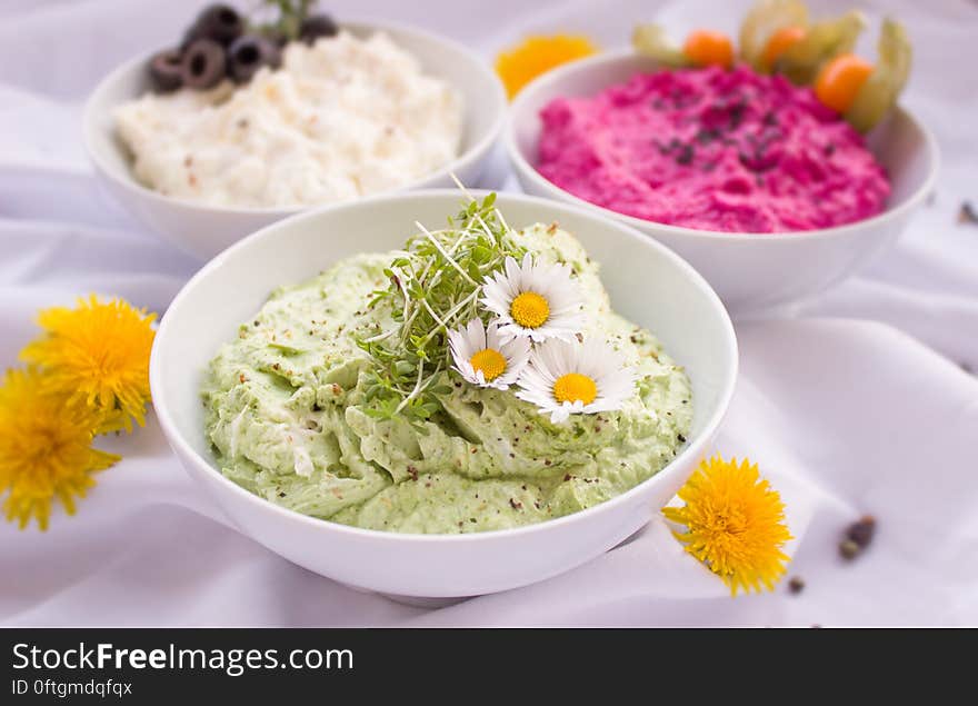 Bowls of dip decorated with flowers on table.