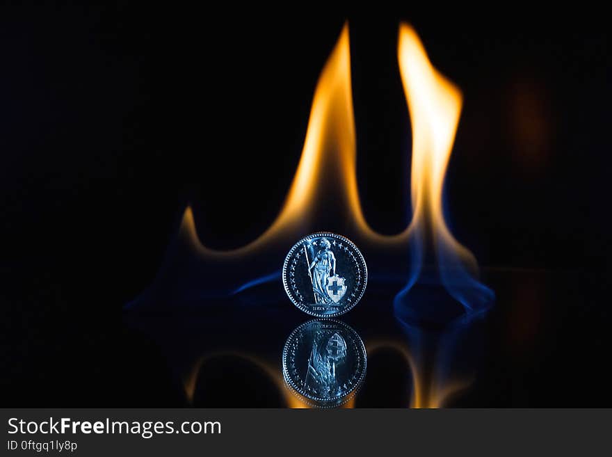 A coin on black background with flames rising on the background. A coin on black background with flames rising on the background.