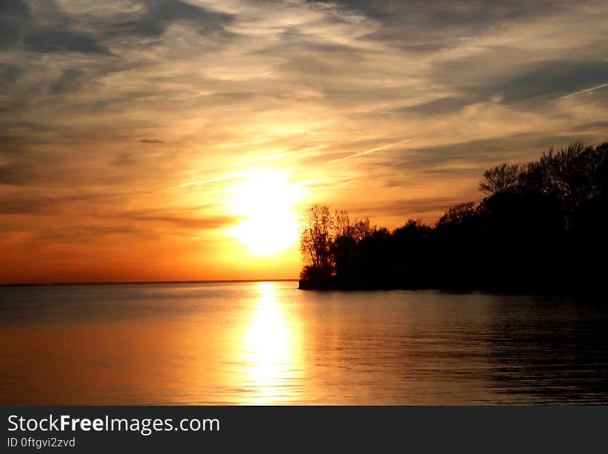 Scenic view of orange sunset and cloudscape along silhouetted ocean coastline. Scenic view of orange sunset and cloudscape along silhouetted ocean coastline.