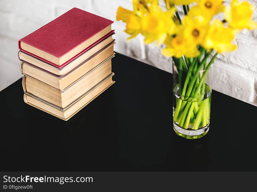 A table with books and yellow daffodils in a vase. A table with books and yellow daffodils in a vase.