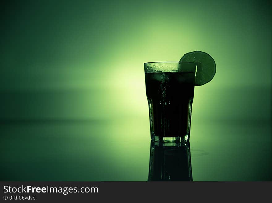 A table glass with a drink and a slice of lemon or lime on a green background. A table glass with a drink and a slice of lemon or lime on a green background.