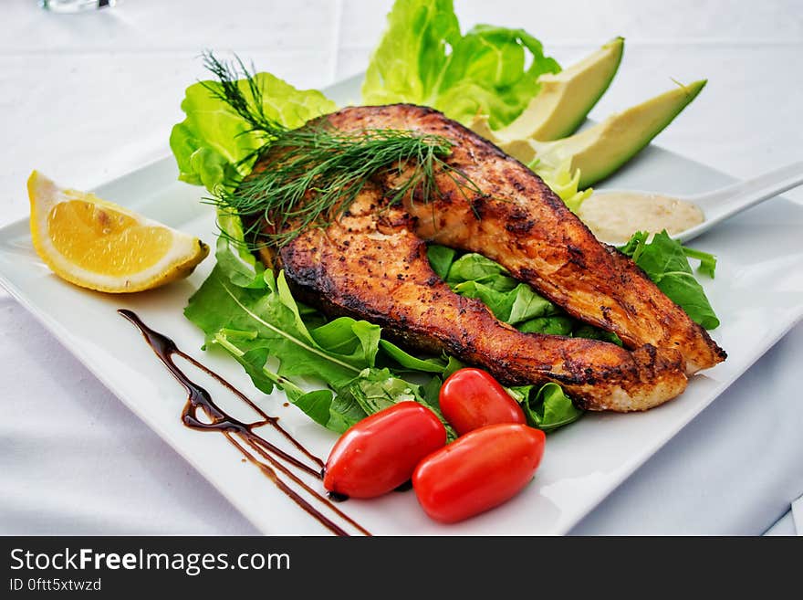 A fried fish medallion on a bed of green salad with avocado and tomatoes. A fried fish medallion on a bed of green salad with avocado and tomatoes.