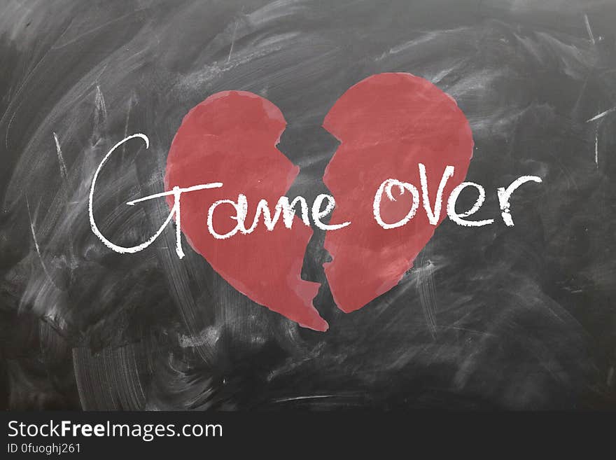 Red broken heart drawn on blackboard with white chalk text graphics game over. Red broken heart drawn on blackboard with white chalk text graphics game over.