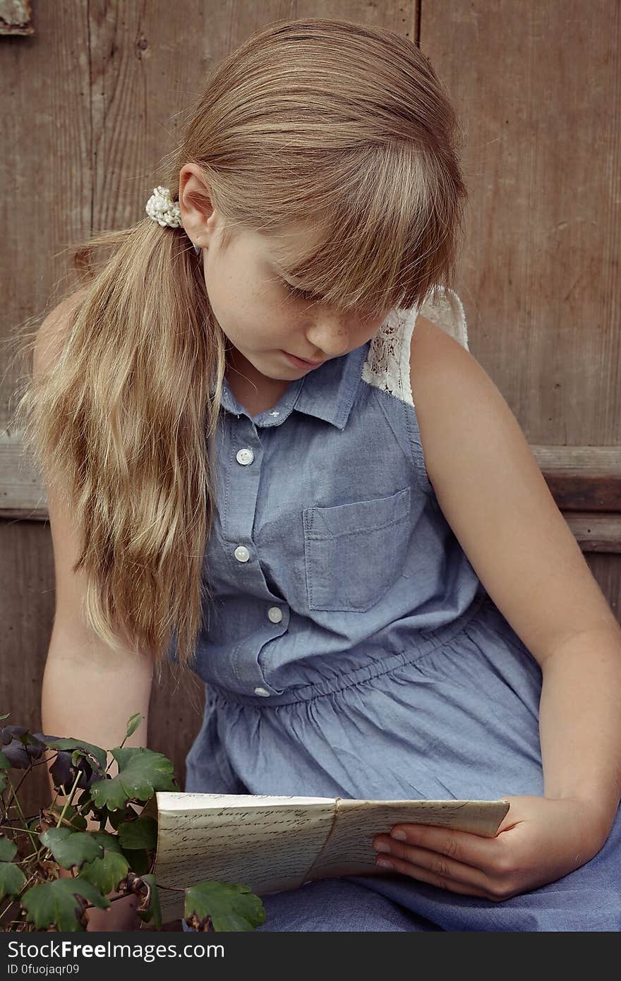 Portrait of young girl in blue dress sitting outdoors in garden reading on sunny day. Portrait of young girl in blue dress sitting outdoors in garden reading on sunny day.