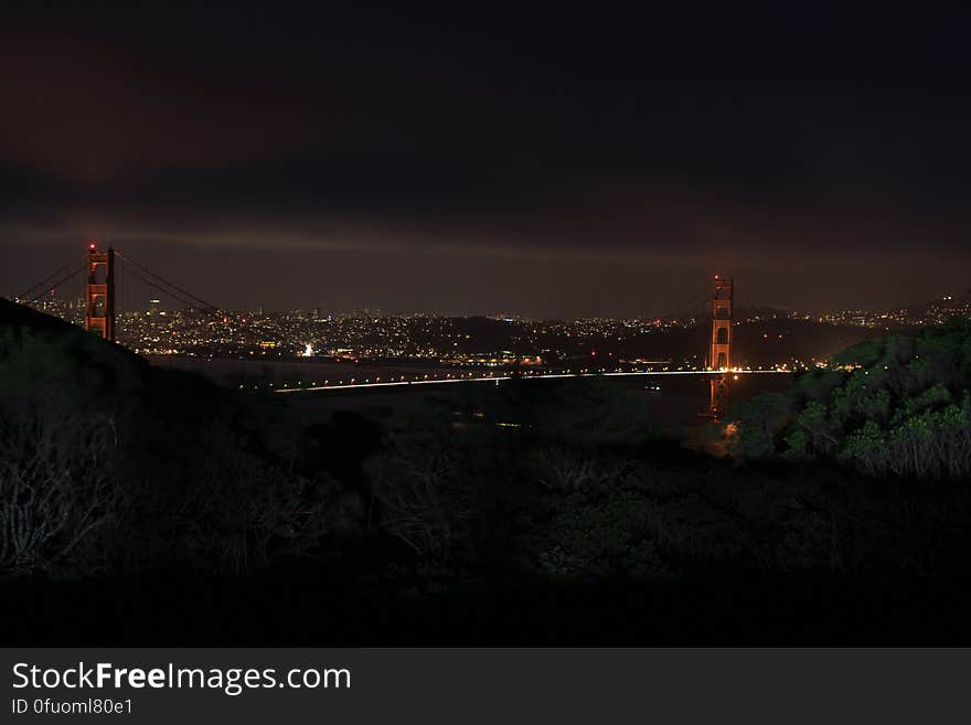 Suspension bridge over river with city skyline in background, night scene. Suspension bridge over river with city skyline in background, night scene.