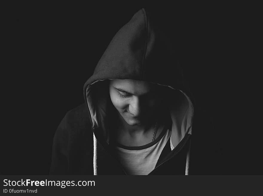 A portrait of a hoodie taken at night with the man wearing a black jacket and white t-shirt giving a threatening impression especially with his eyes downcast.