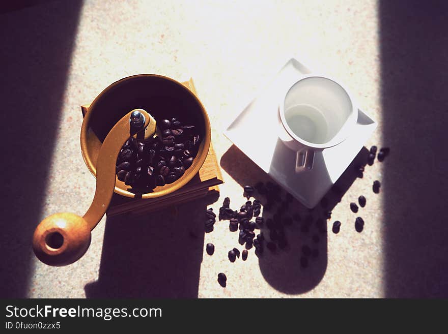 Coffee mill with whole beans next to empty white china cup and sauce in sunlight. Coffee mill with whole beans next to empty white china cup and sauce in sunlight.