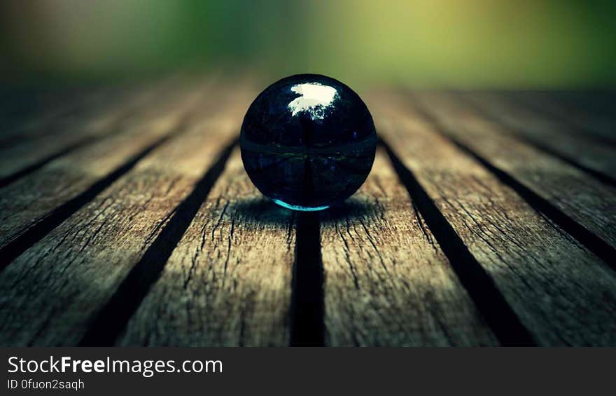 Selective focus on a black marble supported on a series of old wooden planks (table top perhaps) with spaces between each one, blurred background. Selective focus on a black marble supported on a series of old wooden planks (table top perhaps) with spaces between each one, blurred background.