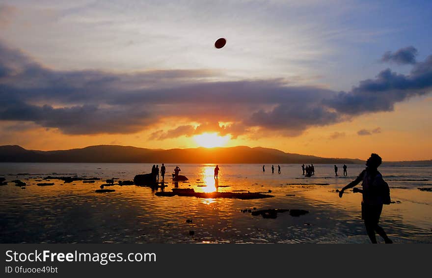 People playing on a beach at sunset.