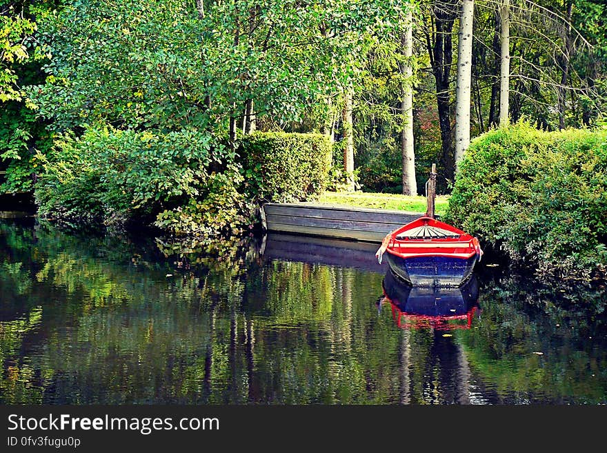 Empty boat moored to banks of lake in green park with trees on sunny day. Empty boat moored to banks of lake in green park with trees on sunny day.