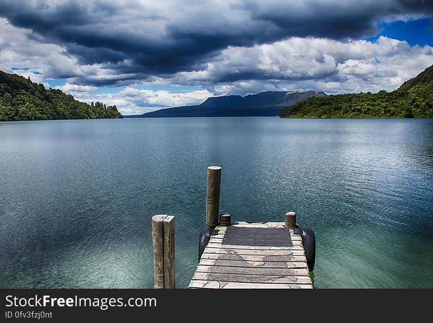 Empty wooden dock along shoreline of lake with cloudy skies. Empty wooden dock along shoreline of lake with cloudy skies.