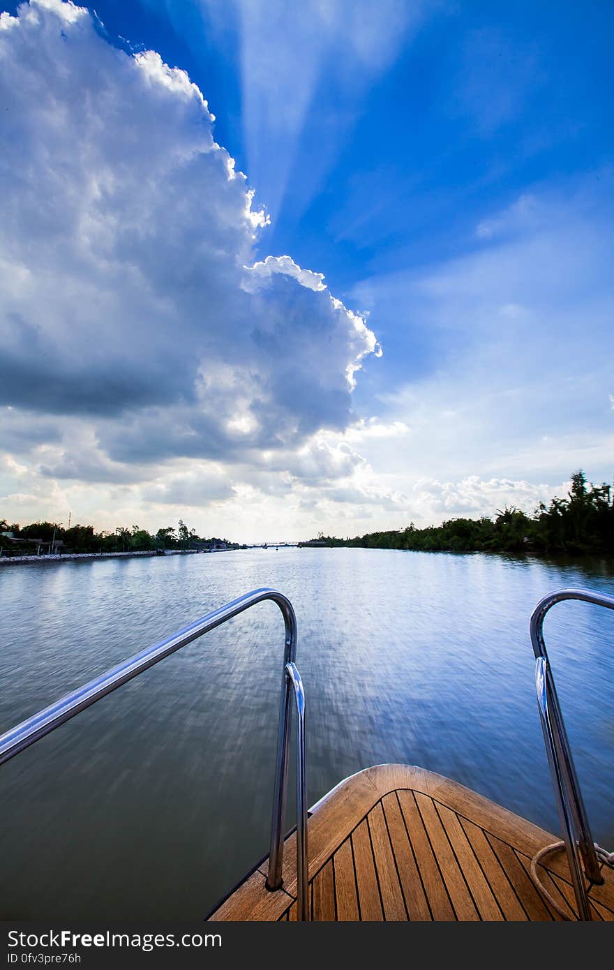 Wooden deck of yacht on blue waters of river against blue skies with white clouds.