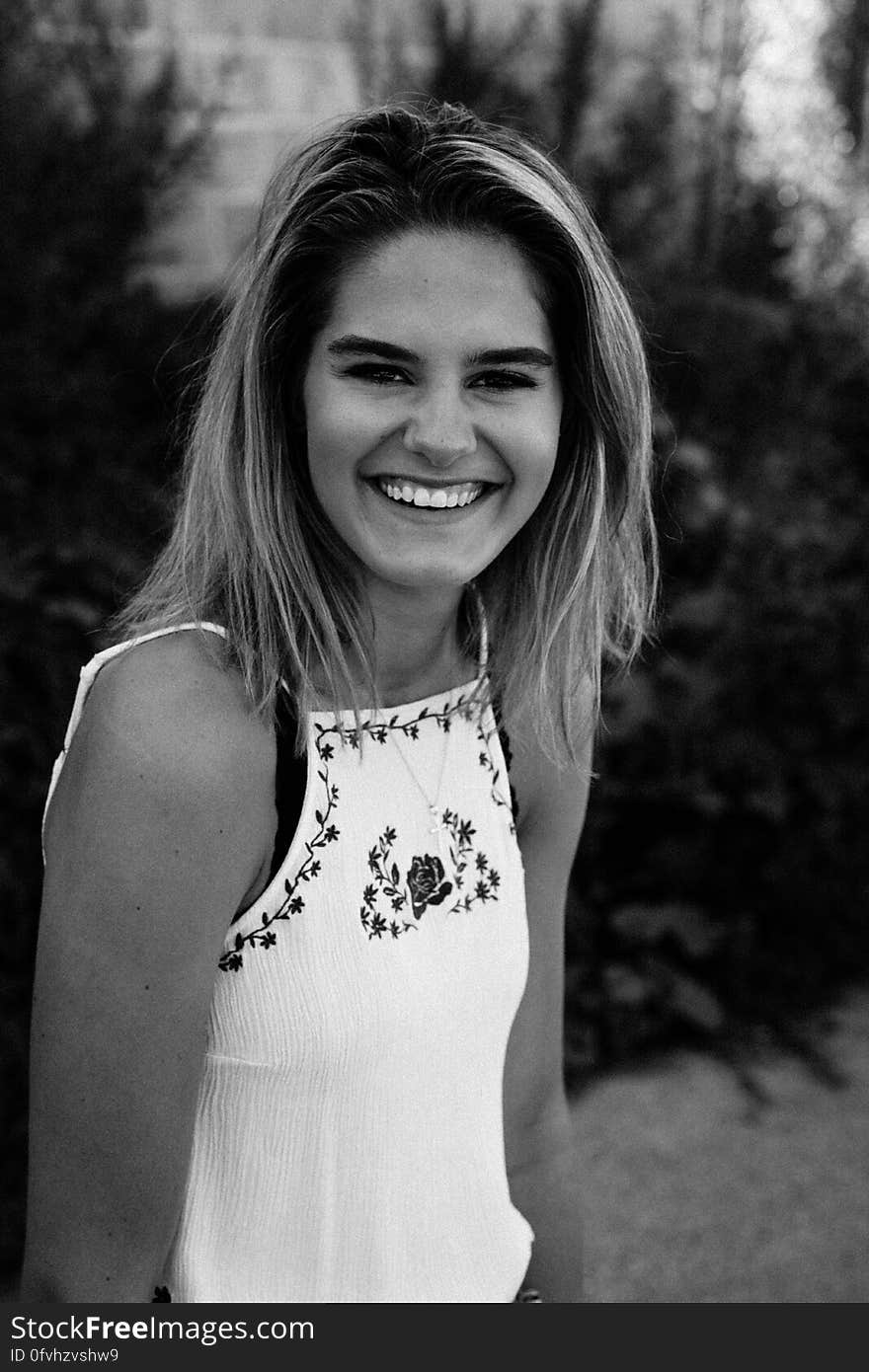 Portrait of young woman with long blond hair wearing white top smiling outdoors in black and white. Portrait of young woman with long blond hair wearing white top smiling outdoors in black and white.