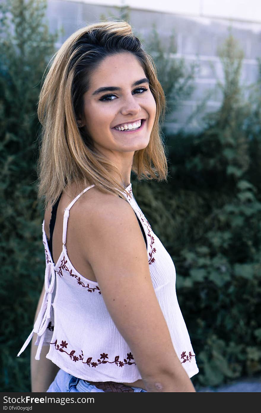 Happy young woman with long blond hair wearing white top and blue jeans standing in garden on sunny day. Happy young woman with long blond hair wearing white top and blue jeans standing in garden on sunny day.