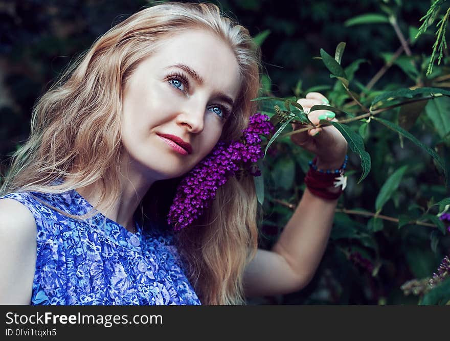 Woman Wearing Blue Floral Sleeveless Dress Smelling Violet Flower