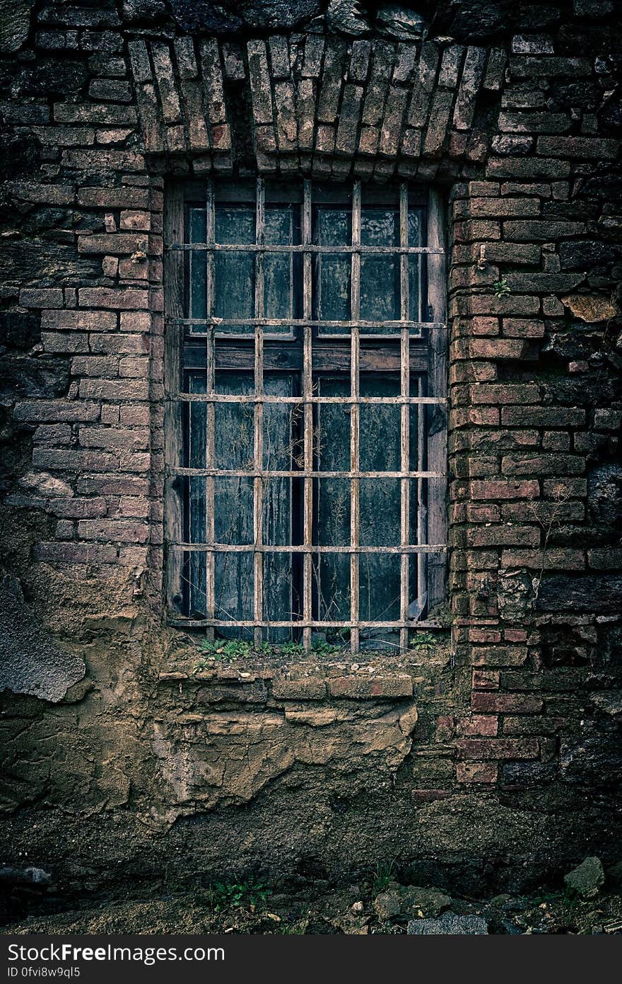 An old, ruined brick wall with a window with metal grids. An old, ruined brick wall with a window with metal grids.