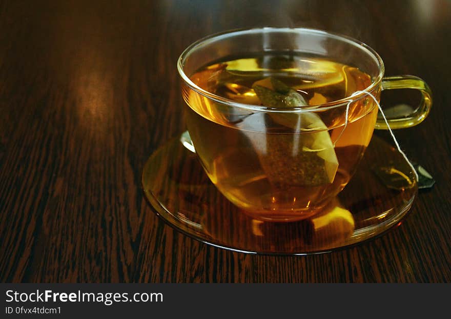 Close up of glass cup and sauce with tea bag and hot beverage on wooden tabletop. Close up of glass cup and sauce with tea bag and hot beverage on wooden tabletop.