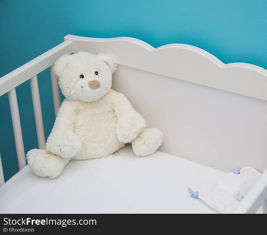 A cute white teddy bear in a crib. A cute white teddy bear in a crib.