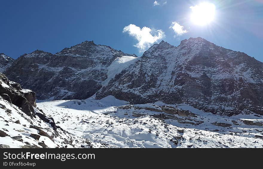 Snow covered mountain peaks against blue skies with sunshine.