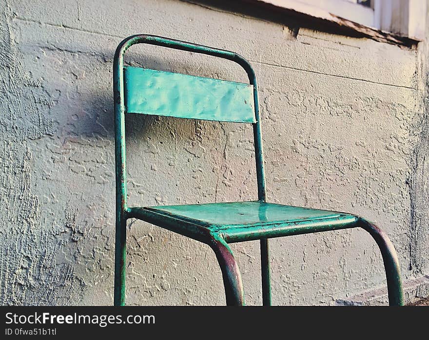 Rusty green painted metal chair against concrete wall outdoors. Rusty green painted metal chair against concrete wall outdoors.