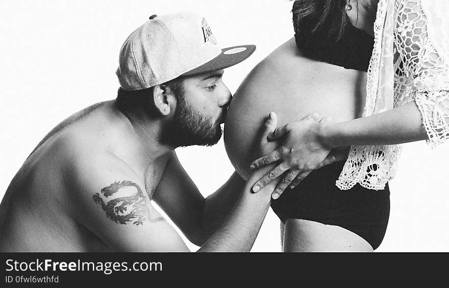 A black and white image of a man kissing the pregnant woman's belly. A black and white image of a man kissing the pregnant woman's belly.