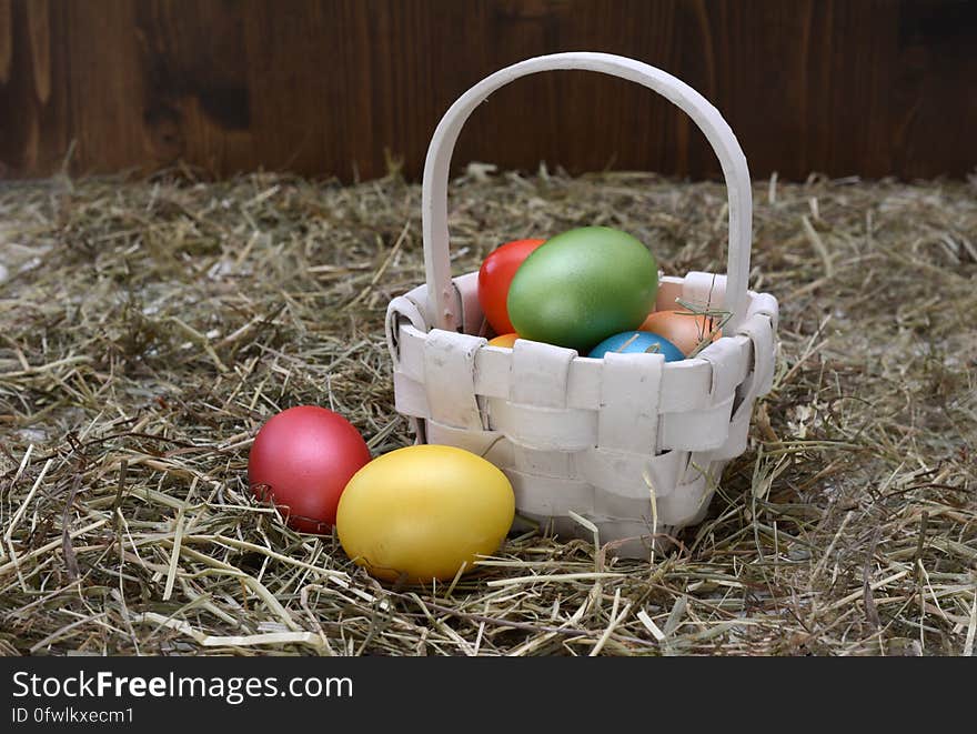 Colorful dyed Easter eggs in white wicker basket in straw of rustic barn. Colorful dyed Easter eggs in white wicker basket in straw of rustic barn.