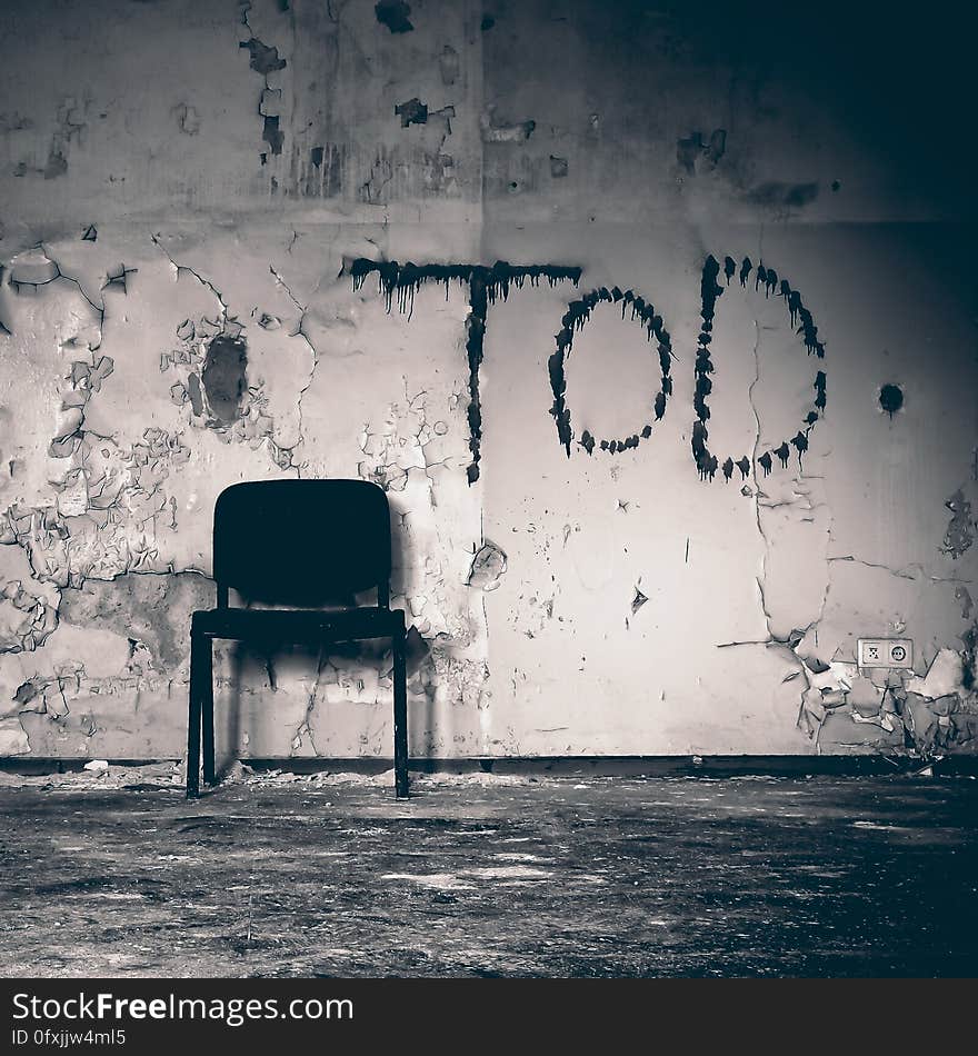 Chair leaning against wall with peeling paint and graffiti in abandoned building in black and white. Chair leaning against wall with peeling paint and graffiti in abandoned building in black and white.