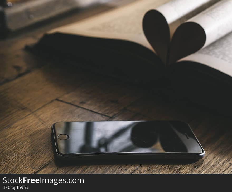 Closeup of smartphone on rustic wooden boards with open book. Closeup of smartphone on rustic wooden boards with open book.