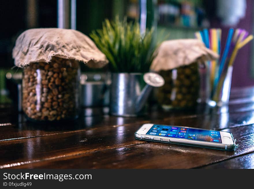 Smartphone on rustic wood tabletop with glass jars and planter. Smartphone on rustic wood tabletop with glass jars and planter.