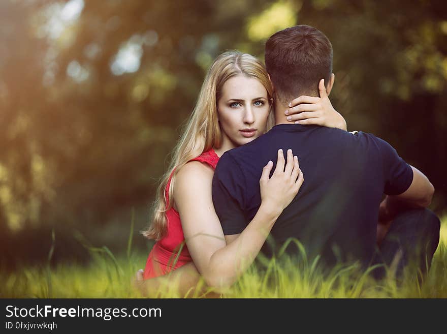 A man and a woman in a park with the woman hugging the man and looking at camera behind his back. A man and a woman in a park with the woman hugging the man and looking at camera behind his back.