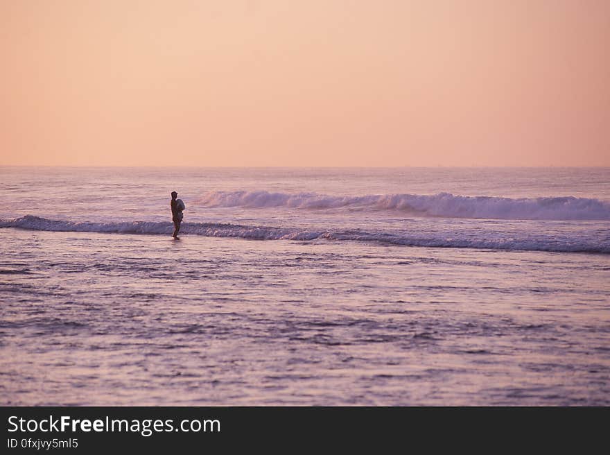 A person standing on the beach at sunset.