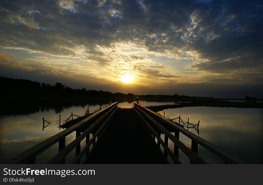 A pontoon over a lake at sunset and the silhouetted coast. A pontoon over a lake at sunset and the silhouetted coast.