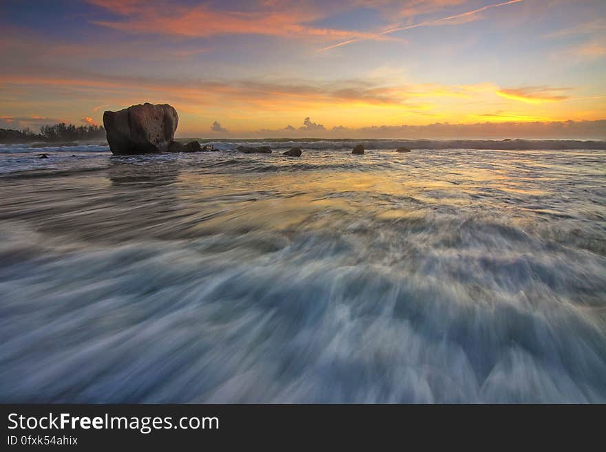 A long exposure of the waves on a beach with a rock at sunset. A long exposure of the waves on a beach with a rock at sunset.