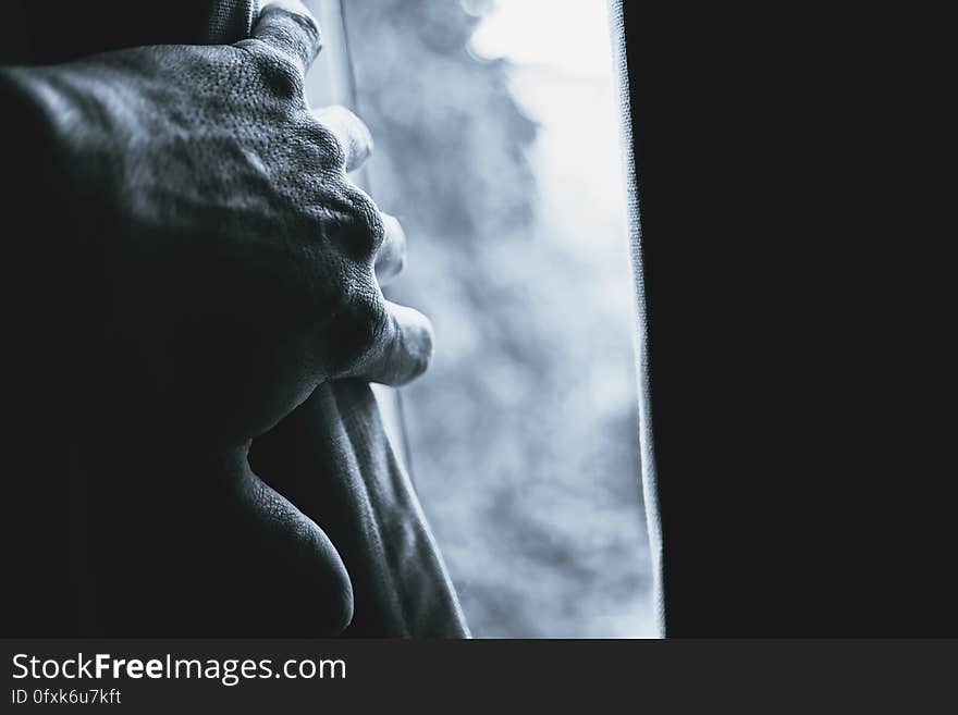 A black and white close up of a man`s hand opening a curtain. A black and white close up of a man`s hand opening a curtain.