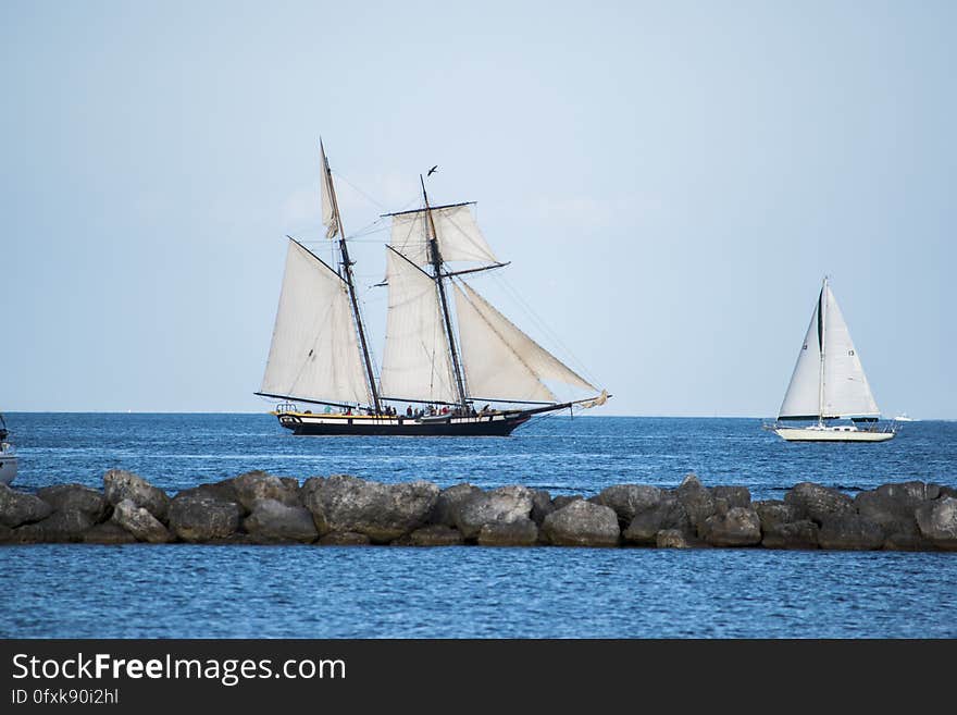 Sailboats behind rocky causeway and open sea in the background.