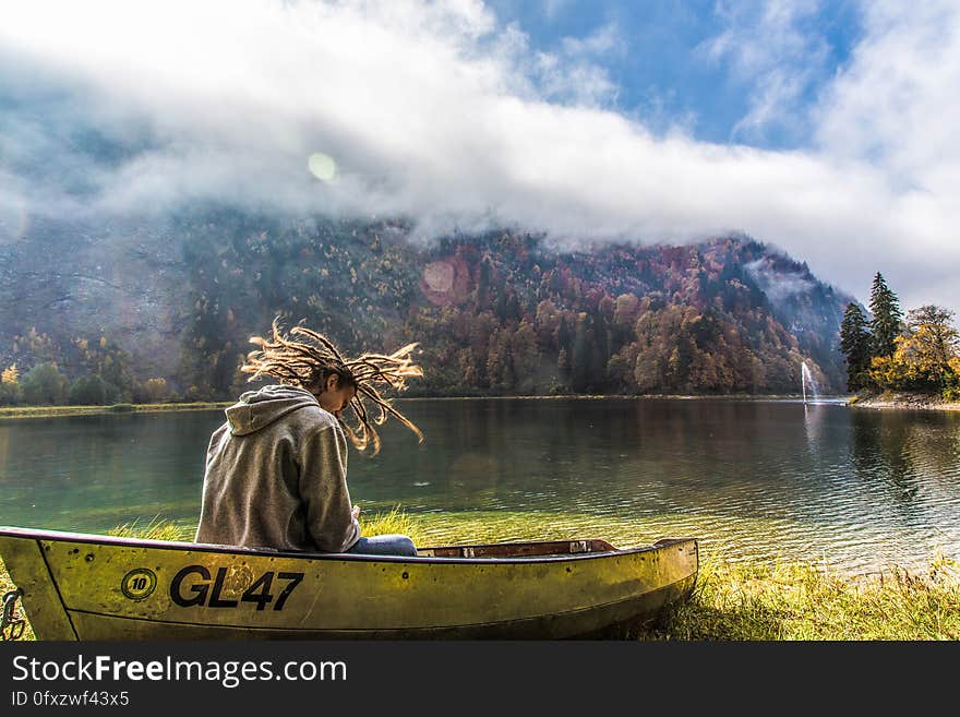 Man in Brown Hoodie Sitting on Yellow Paddle Boat Beside Lake Behind Hills during Daytime