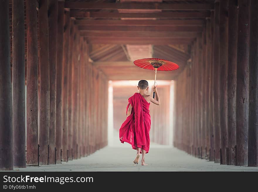 Young male monk in red robes with red umbrella walking down hallway. Young male monk in red robes with red umbrella walking down hallway.