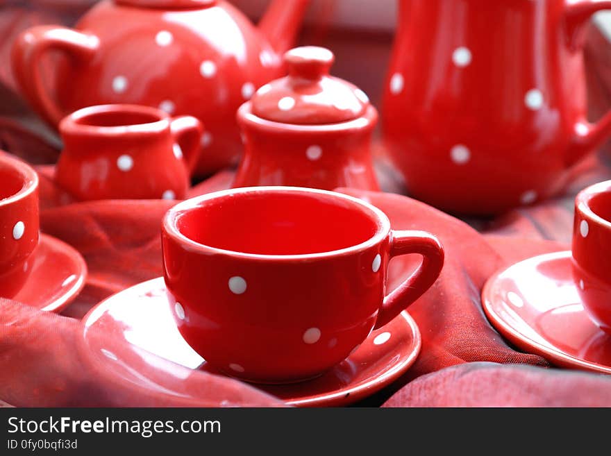 Red cups, saucers, milk jug, sugar bowl, coffee pot, all matching in red with white spots and selective focus on just one cup. Red cups, saucers, milk jug, sugar bowl, coffee pot, all matching in red with white spots and selective focus on just one cup.