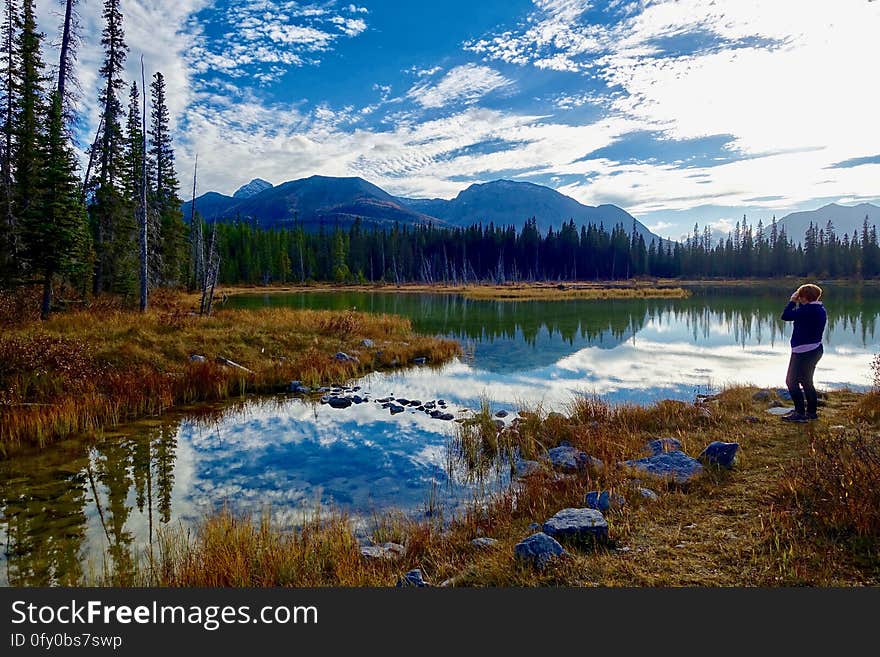 Person relaxing by countryside lake in autumn with mountains in background.