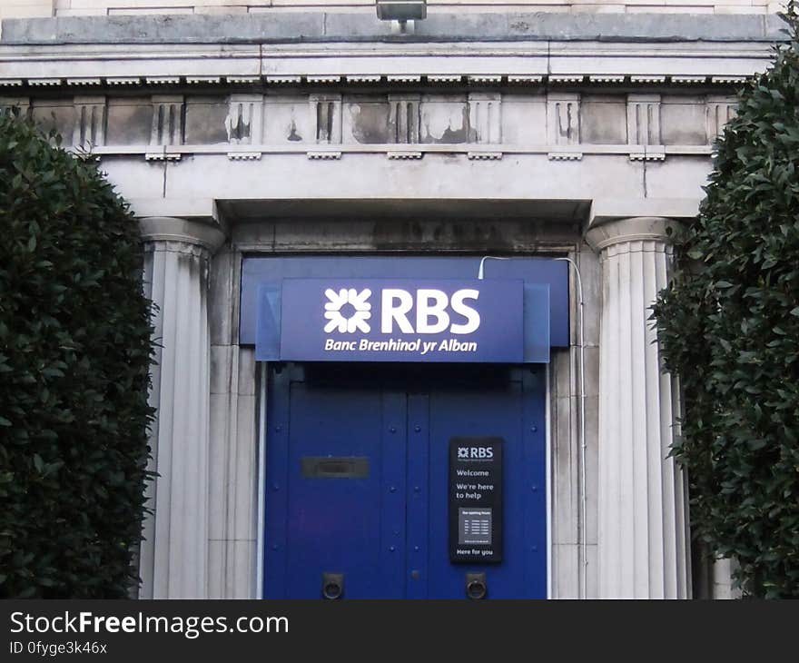 A Welsh version of the RBS name for a Welsh branch in 2011. Destined to be a thing of the past, as the English and Welsh branches of RBS are due for sell-off. For the uninitiated, the government support package that stopped RBS collapsing in 2009 resulted in a requirement that the 300-odd branches of RBS in England and Wales be sold off. The plan has changed many times. A planned sell-off to Santander collapsed. Then RBS decided to create and float a new standalone bank using these branches, the NatWest branches in Scotland and the long-dormant Williams and Glyn brand they owned. By summer 2016, questions about the financial viability of the proposed new business and the difficulty of creating a new IT infrastructure saw the plan shelved. Branches like this one are now back on the market - and may yet end up with Santander, five years later on!. A Welsh version of the RBS name for a Welsh branch in 2011. Destined to be a thing of the past, as the English and Welsh branches of RBS are due for sell-off. For the uninitiated, the government support package that stopped RBS collapsing in 2009 resulted in a requirement that the 300-odd branches of RBS in England and Wales be sold off. The plan has changed many times. A planned sell-off to Santander collapsed. Then RBS decided to create and float a new standalone bank using these branches, the NatWest branches in Scotland and the long-dormant Williams and Glyn brand they owned. By summer 2016, questions about the financial viability of the proposed new business and the difficulty of creating a new IT infrastructure saw the plan shelved. Branches like this one are now back on the market - and may yet end up with Santander, five years later on!