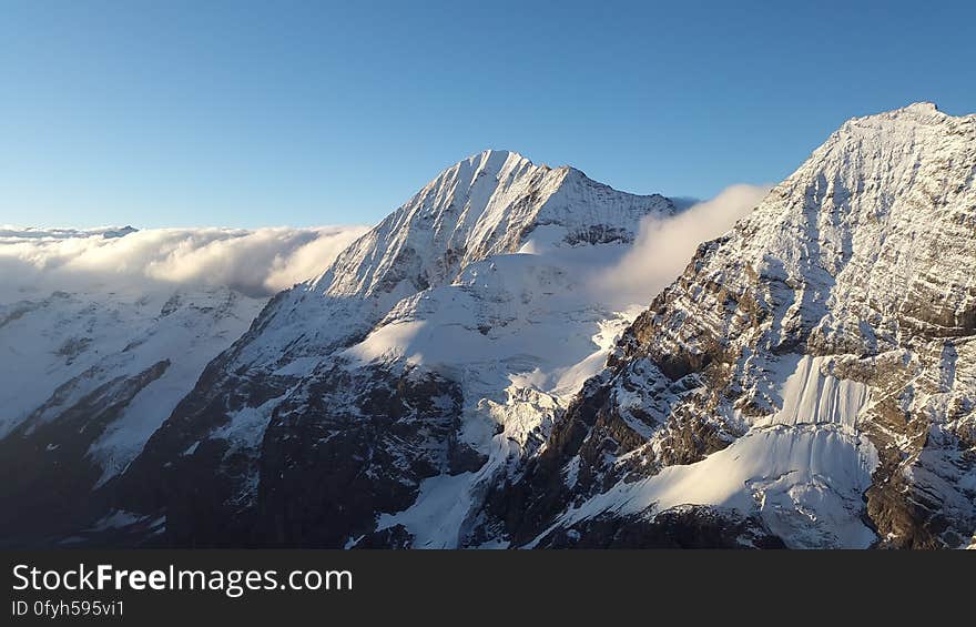 Snow on windswept jagged mountain peaks, background of clear blue sky. Snow on windswept jagged mountain peaks, background of clear blue sky.