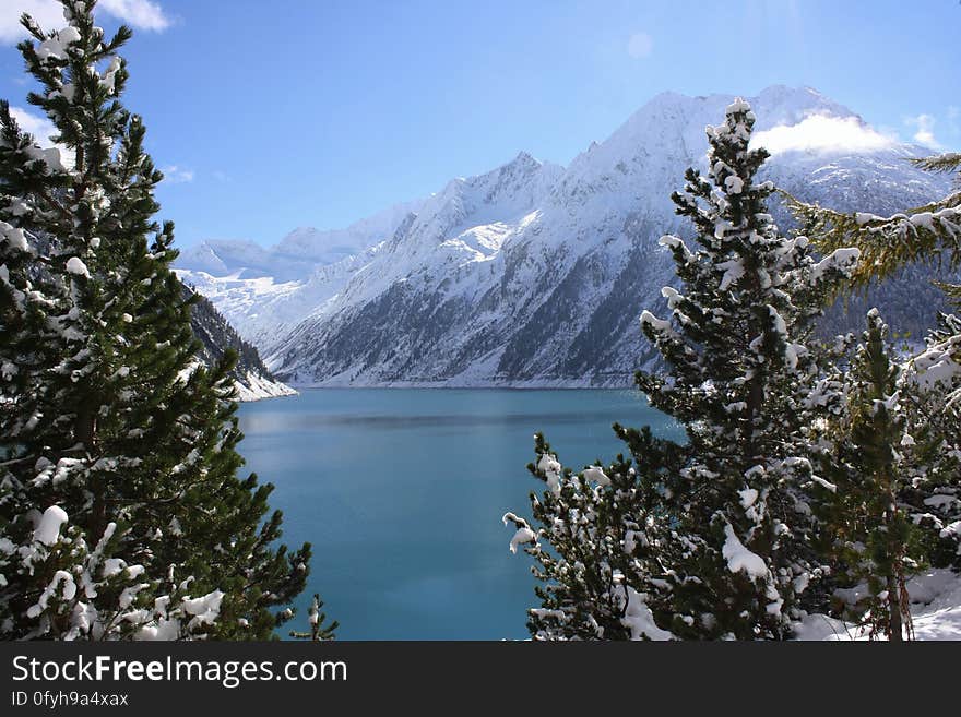 Scenic view of alpine lake and forest with snow capped mountains in background. Scenic view of alpine lake and forest with snow capped mountains in background.