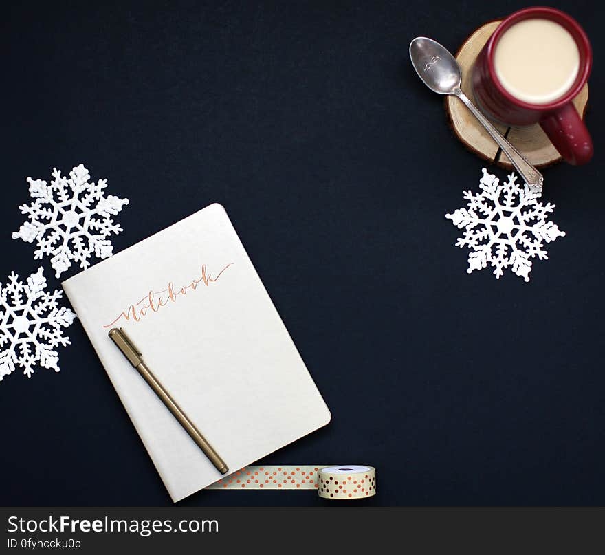 A notebook with a pen, a cup of coffee with milk, duct tape, and snowflake decorations. A notebook with a pen, a cup of coffee with milk, duct tape, and snowflake decorations.