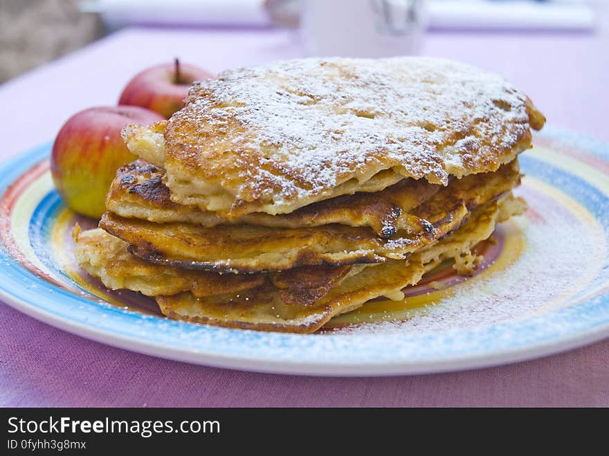 Apples and pancakes dusted with icing sugar on a red white and blue plate, blurred background. Apples and pancakes dusted with icing sugar on a red white and blue plate, blurred background.