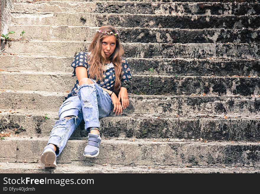 A woman wearing torn jeans and wreath of flowers sitting on concrete stairs. A woman wearing torn jeans and wreath of flowers sitting on concrete stairs.