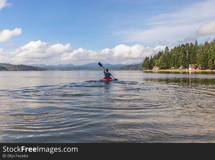 A person canoeing on a lake. A person canoeing on a lake.