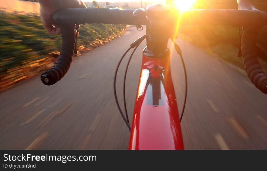 Hands of person riding racing bicycle on road with sun glistening off handlebars.