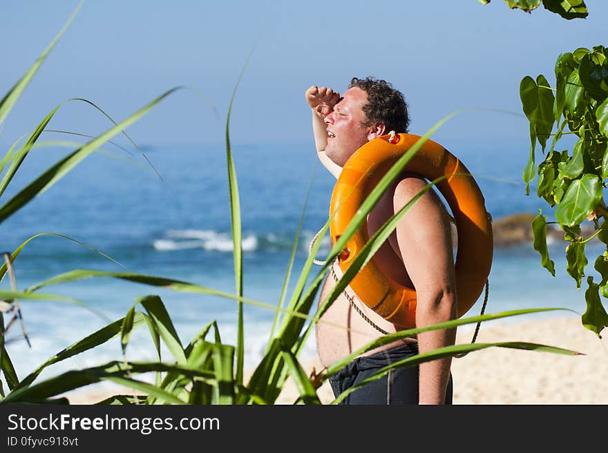 Man relaxing on tropical beach with inflatable ring over shoulder.