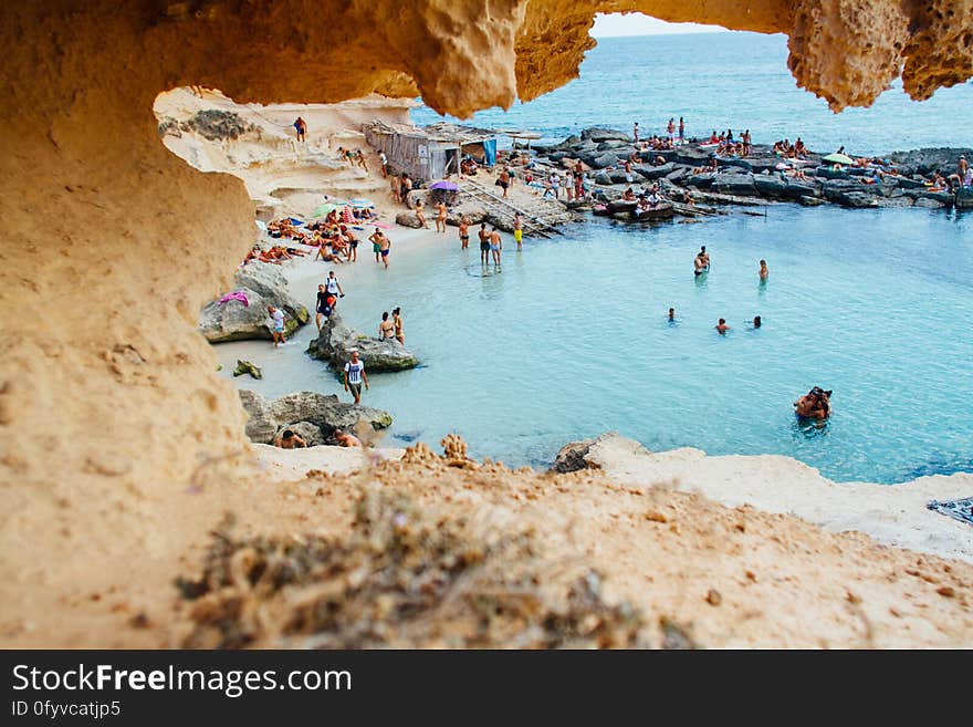 Tourists swimming in blue cove on the coastline of Spain, with overhanging cave rock formation in foreground.