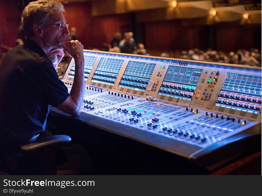 Man sitting at electronic sound mixing console inside theater. Man sitting at electronic sound mixing console inside theater.